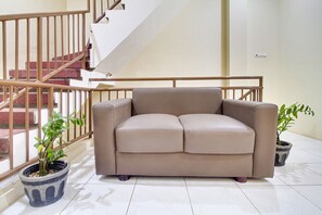 A beige sofa in a room with tiled flooring, a staircase with wooden railings, and two potted plants. - OYO 2354 3 Point Residence (Surabaya)