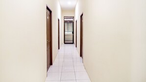 A narrow hallway with white tiled floors and wooden doors on both sides, leading to a room with a window and curtains. - OYO 2354 3 Point Residence (Surabaya)