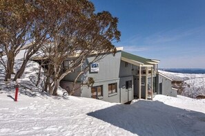 A building with a green roof, a sign indicating a public restroom, and a snow-covered landscape. - Alpine Heights 21 (Hotham Heights)