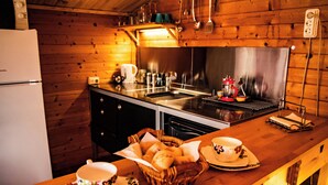 Eine Holzhütte mit Küche, ausgestattet mit einem Edelstahl-Spülbecken, einem Kühlschrank und einem Essbereich, der ein Brotkörbchen, eine Tasse und einen Untertasse zeigt.