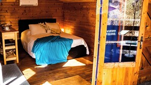 Ein Schlafzimmer einer Holzhütte mit einem Bett, einem Nachttisch und einem Fenster.