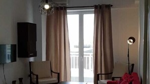 A living room with a red sofa, a TV mounted on the wall, a ceiling light, and a view of the outdoors through large windows.
