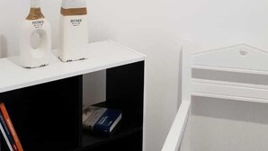A room with a white desk, two white objects on it, a bookshelf, a crib, and two framed pictures on the wall.