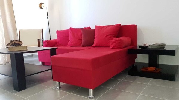 Un salon moderne avec un canapé rouge, une table basse noire et une petite table d’appoint noire sur laquelle se trouve un bol.