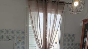 A dining area with a round table, four chairs, a decorative table runner, and a window with sheer curtains.