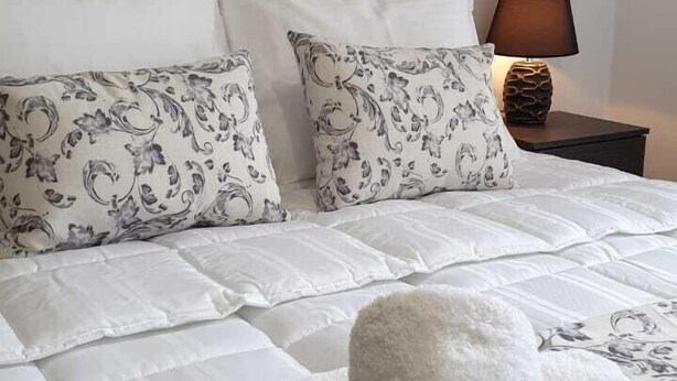 A neatly made bed with floral-patterned bedding, a headboard, and two pillows.