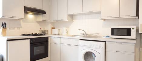 A modern kitchen with white cabinetry, a built-in oven, a microwave, a dishwasher, and a washing machine.