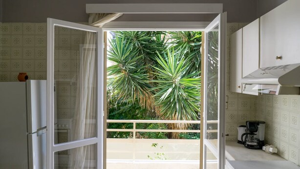 A kitchen with white cabinets, a coffee maker, and a view of a balcony with plants. - Cozy Flat Kika's Heraklion CITY CENTRAL (Heraklion)