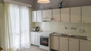 A kitchen with white cabinets, a stove, a sink, and a window with sheer curtains. - Cozy Flat Kika's Heraklion CITY CENTRAL (Heraklion)