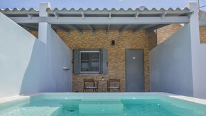 A small, enclosed swimming pool with a tiled deck, two chairs, and a window with shutters. - Avgerinos Deluxe Rooms (Milos)