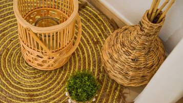 A woven basket with a glass container, a small potted plant, and a woven vase on a woven mat.