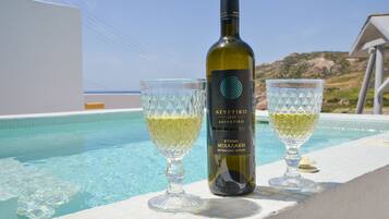 Une bouteille de vin et deux verres posés sur le bord d’une piscine, offrant une vue dégagée sur la mer et les collines en arrière-plan.