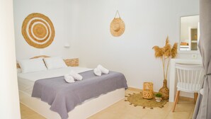 A neatly arranged bedroom with a bed, bedside table, chair, and decorative items. - Avgerinos Deluxe Rooms (Milos)