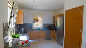 A modern kitchen with wooden cabinets, stainless steel appliances, and a window with a view of a rocky landscape. - Luxury Villa Apollon Private Pool & Amazing View (Malevizi)