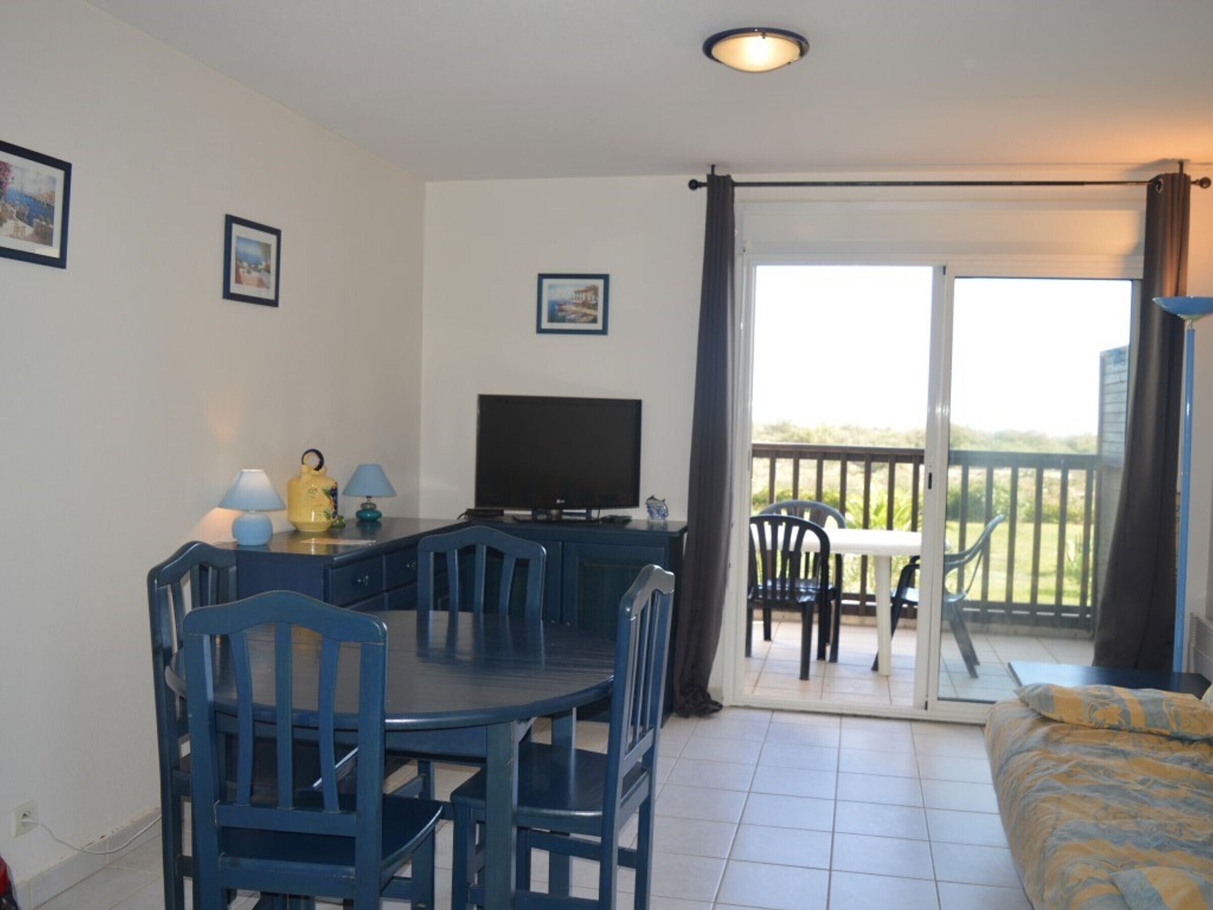 Une pièce comprenant une table à manger, des chaises, un téléviseur et un balcon avec une table et des chaises.