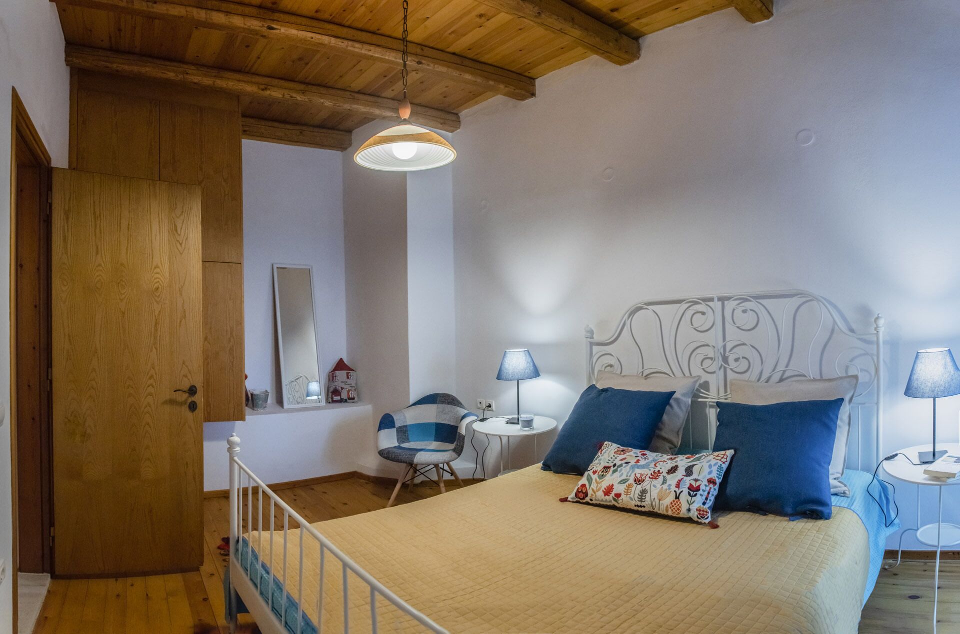 A bedroom with a bed, bedside lamps, a chair, a small table, and a wooden door.