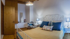 Un dormitorio con cama, lámparas de noche, una silla, una mesita y una puerta de madera.