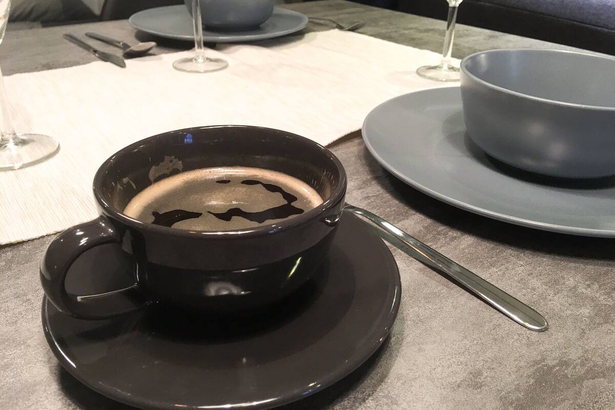 A table with a black cup of coffee, a spoon, and a plate.