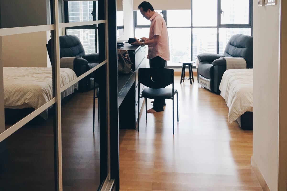 A modern hotel room with a large sliding door, a desk, two beds, and a view of the city through large windows.
