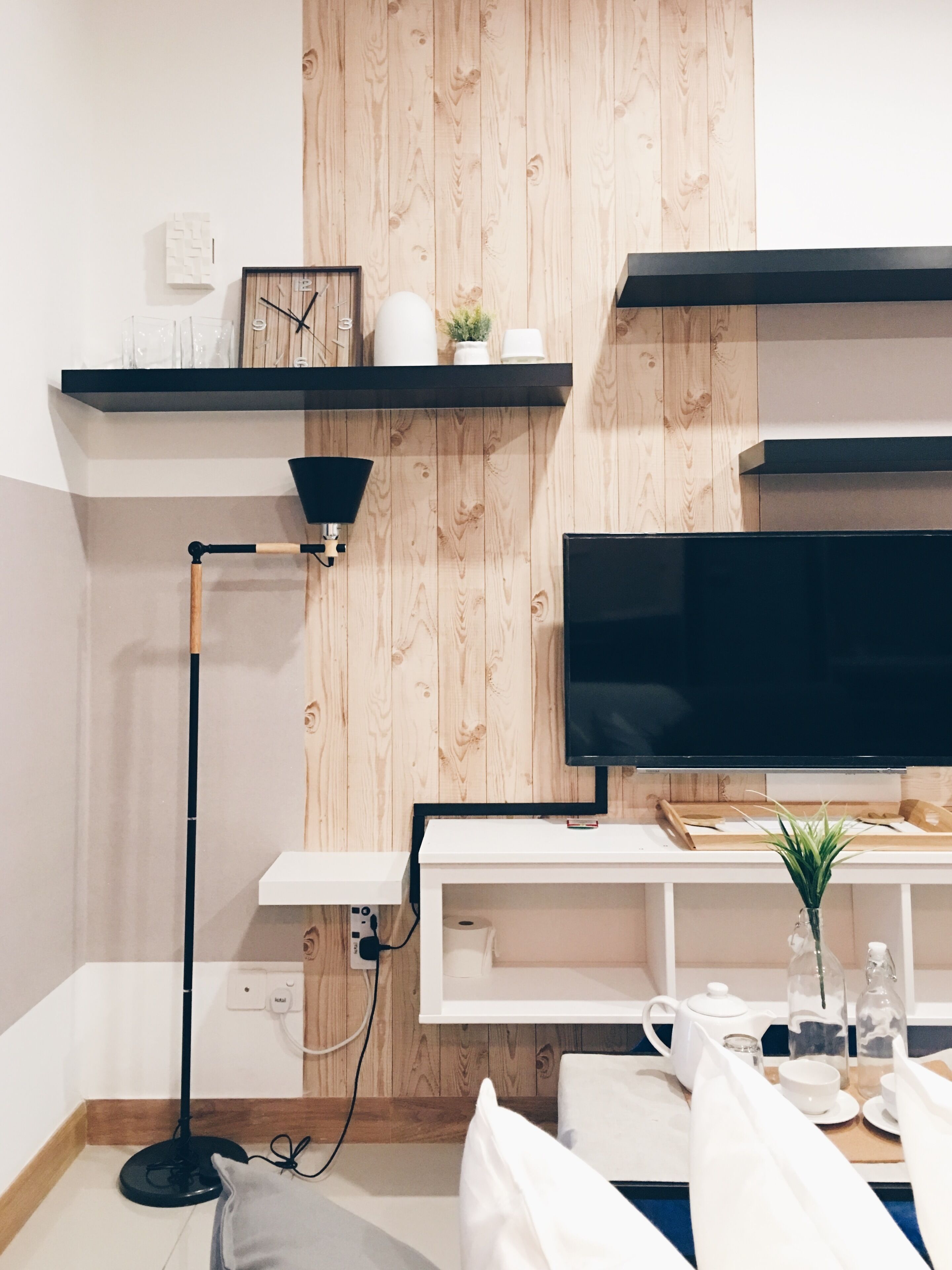 Een moderne woonkamer met een houten wand, een flatscreen televisie, een vloerlamp en een witte salontafel met een plant.