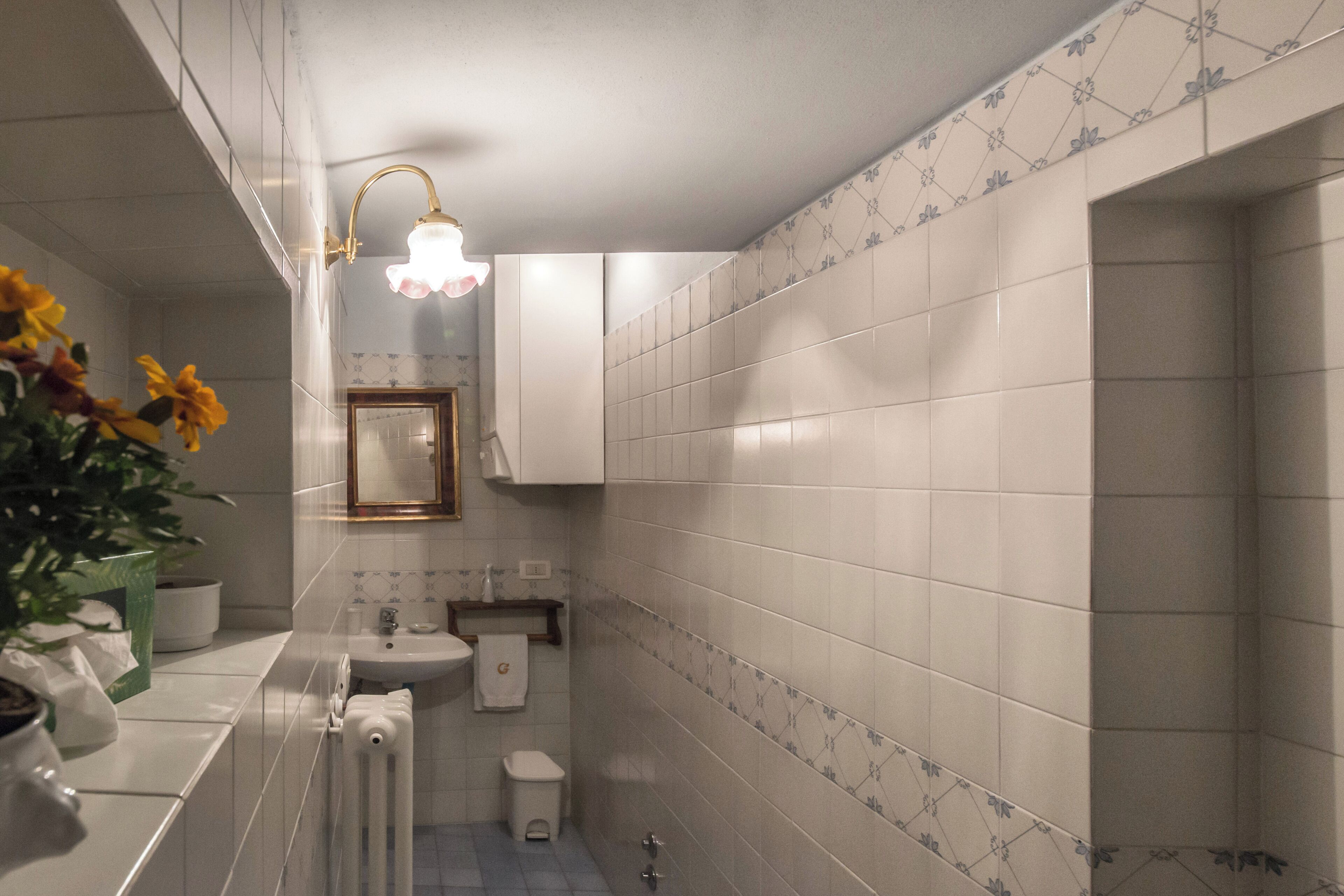 A bathroom with white tiles, a sink, a toilet, and a shower.
