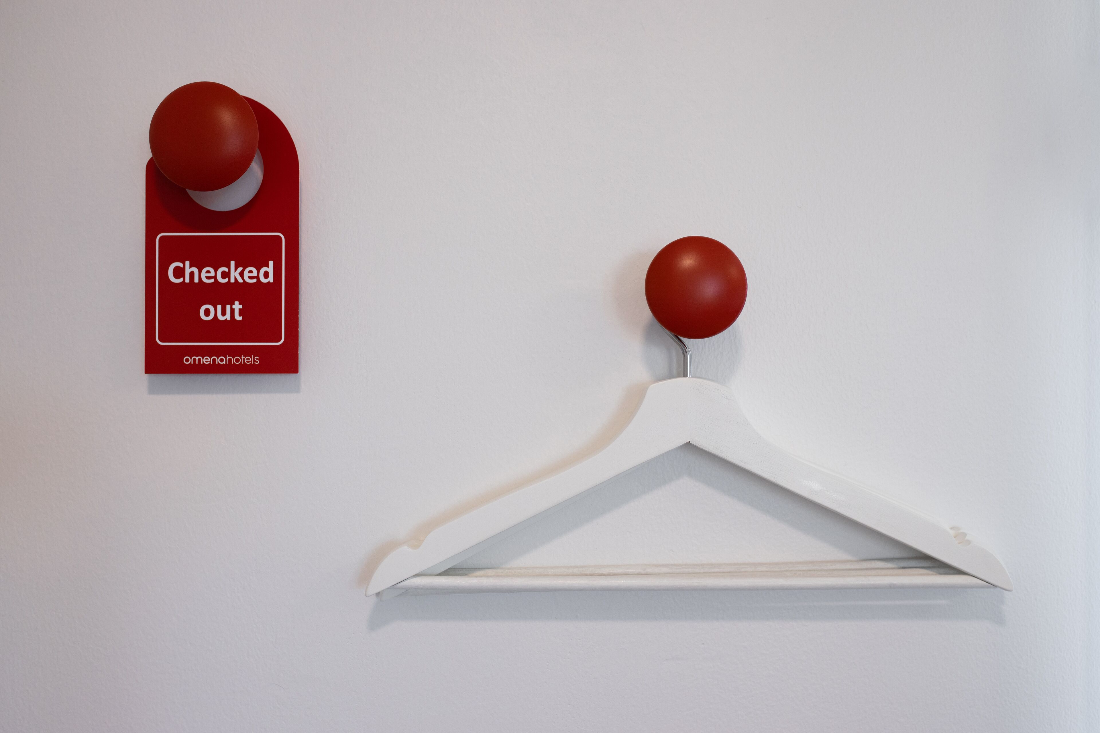 Um sinal vermelho com a inscrição 'Check-out' e um gancho branco na parede.