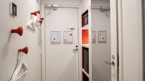 A hotel room with a white door, a red shelf, and multiple emergency exit signs on the wall. - Omena Hotel Vaasa Espen (Vaasa)