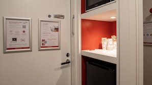 A hotel room with a white door, two framed informational posters, a microwave above the door, and a red wall. - Omena Hotel Vaasa Espen (Vaasa)