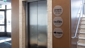 An elevator with a metallic interior and a beige wall with three circular signs indicating hotel names. - Omena Hotel Vaasa Espen (Vaasa)
