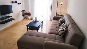 Una sala de estar con un sofá, un televisor, una mesa de centro y una silla.