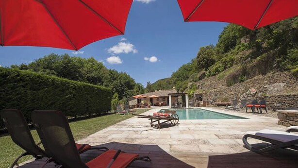 A pool area with lounge chairs and umbrellas, surrounded by a stone deck and a view of a hillside. - Mulino Cintoia Chianti Toscana Pool, Sauna and Jacuzzi Experience (Greve in Chianti)