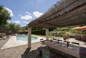 Ein Außenpoolbereich mit überdachter Terrasse, Steinboden und Essbereich mit Tischen und Stühlen.