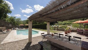 An outdoor pool area with a covered patio, stone flooring, and a dining setup with tables and chairs. - Mulino Cintoia Chianti Toscana Pool, Sauna and Jacuzzi Experience (Greve in Chianti)