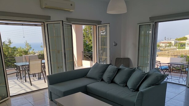 A modern living room with a grey sectional sofa, a white coffee table, and a view of the sea through large glass doors. - Luxury Villa Zen Amazing View Near The Sea (Hersonissos)
