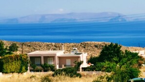 A house with a flat roof, a chimney, and a satellite dish. It is surrounded by greenery and located near a coastline with mountains in the distance. - Luxury Villa Zen Amazing View Near The Sea (Hersonissos)
