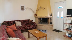 A living room with a sofa, a coffee table, a fireplace, a TV, and a bookshelf. - Amazing House Erato On The Sea South Creta (Archanes-Asterousia)