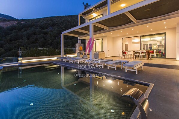 Un área de piscina moderna al aire libre con sillones de descanso y zona de comedor, rodeada por un paisaje montañoso.