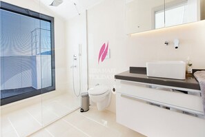 Een moderne badkamer met een douchecabine van glas, een wit toilet en een wastafel met spiegel en aanrecht.