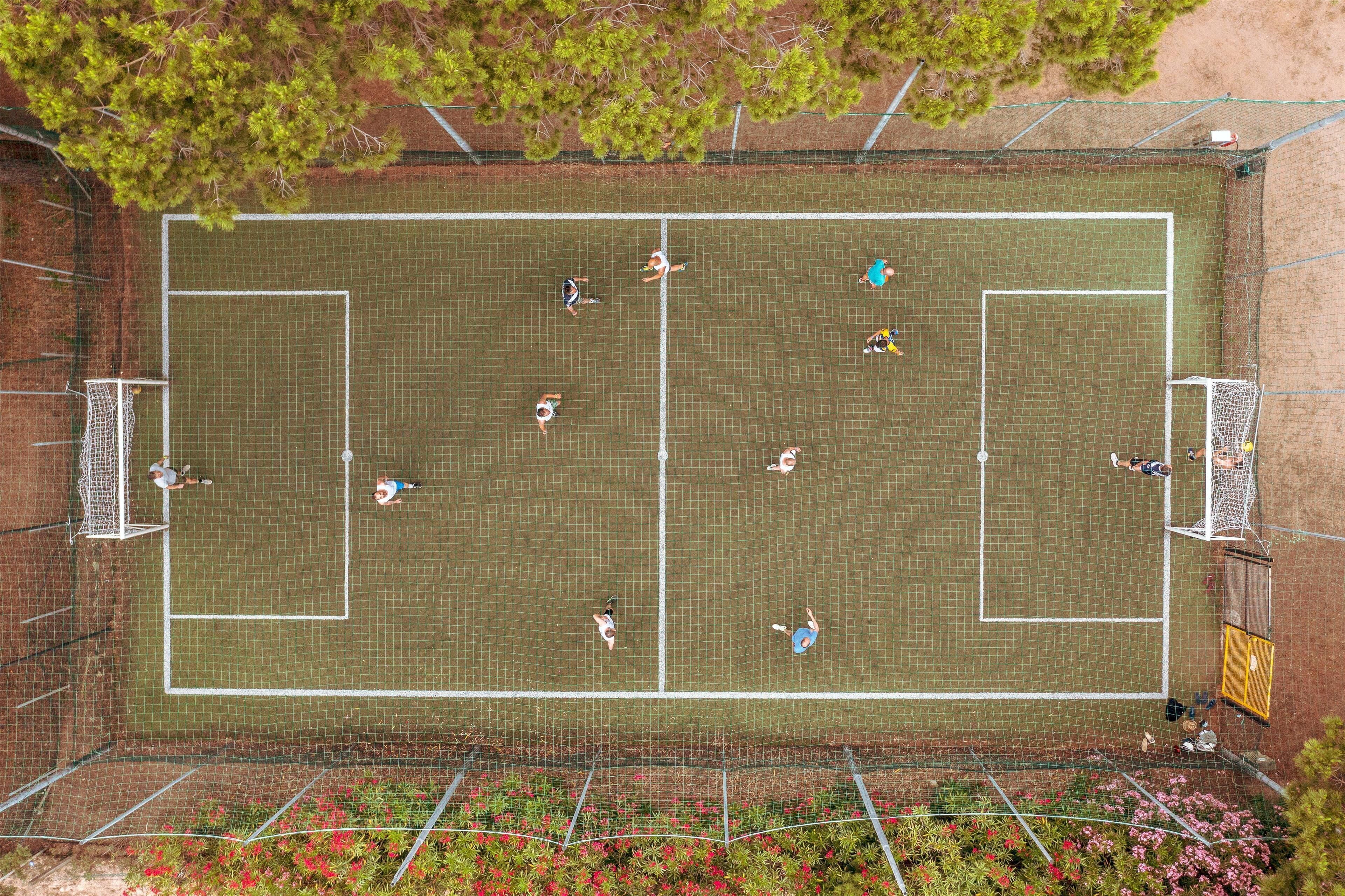 An aerial view of a tennis court with players, two goals, and surrounding greenery.