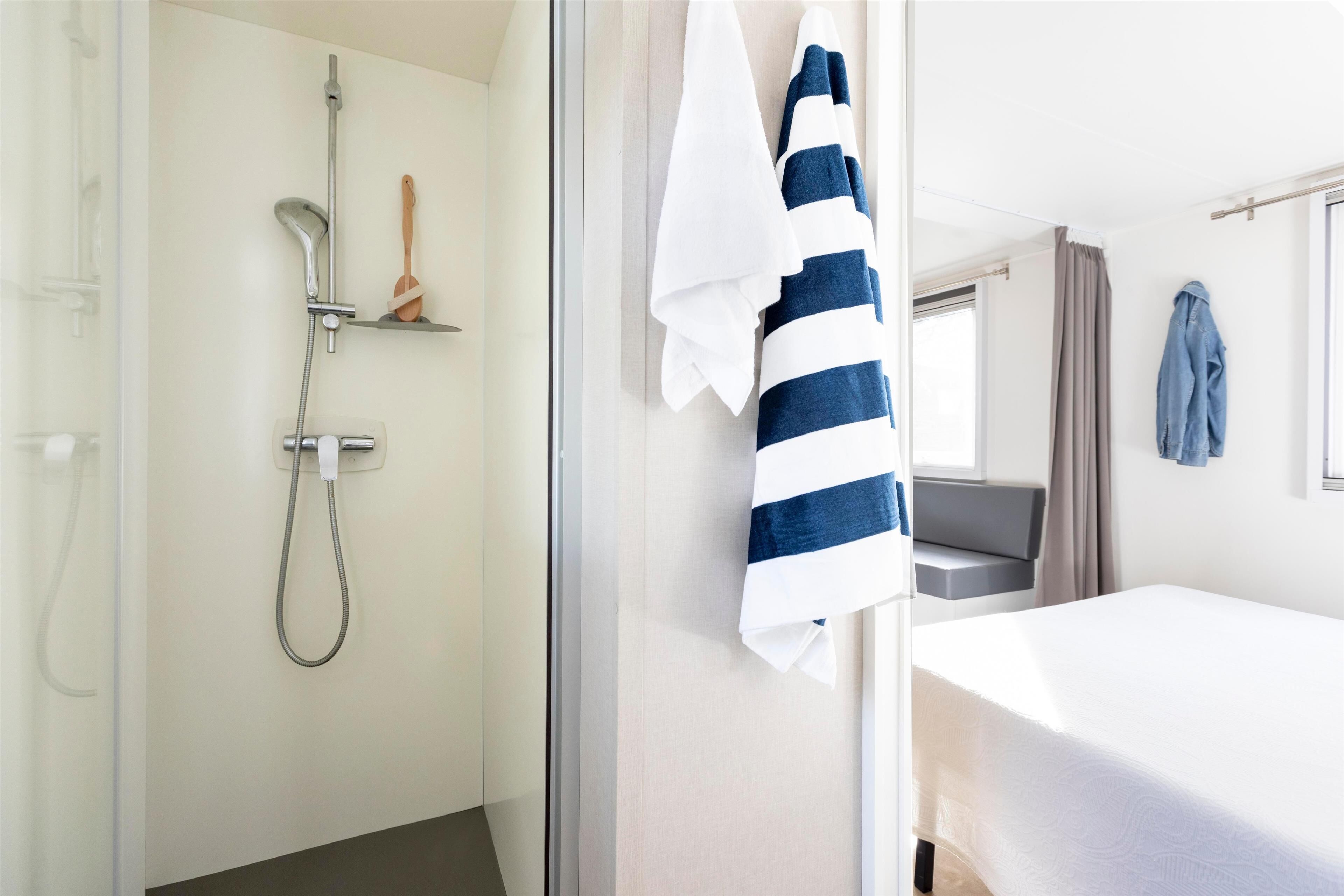 Ein Hotelzimmer mit Dusche, einem Bett, einem Fenster mit Vorhängen und einem Handtuchhalter.