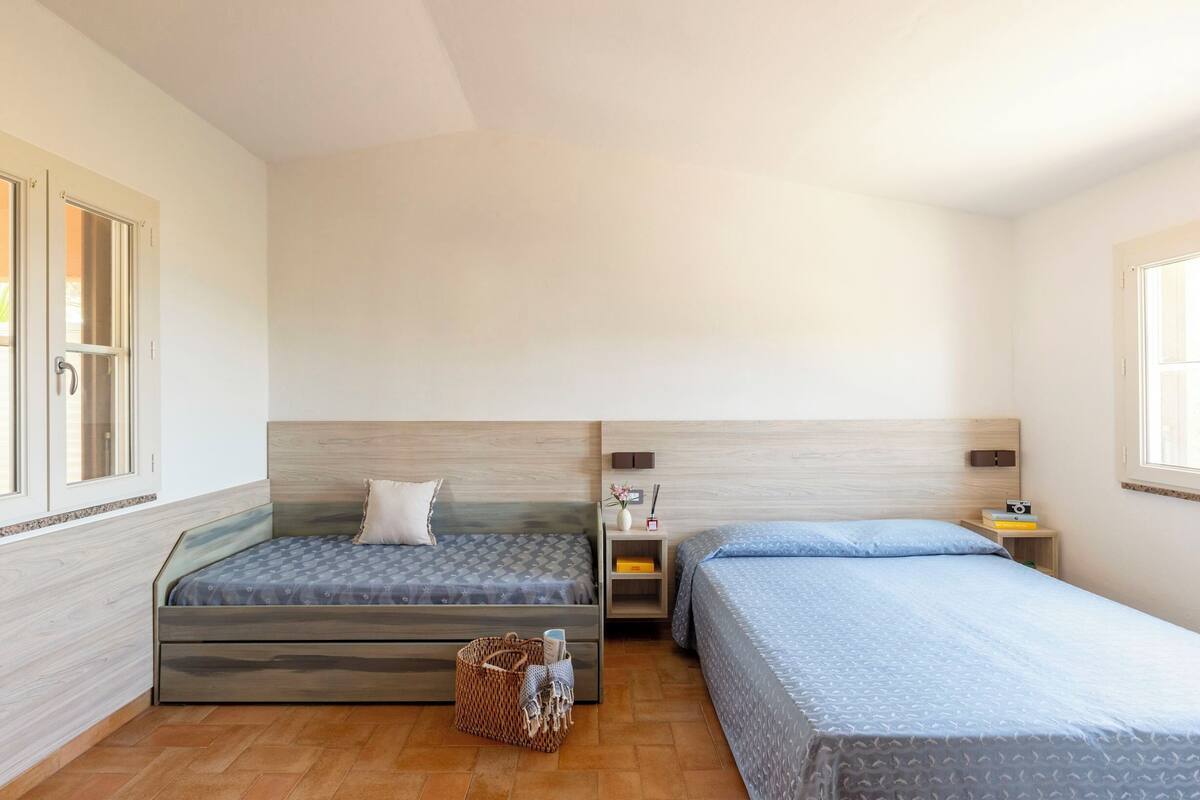 Une chambre avec deux lits, une tête de lit en bois, une table de chevet avec une lampe et une fenêtre.