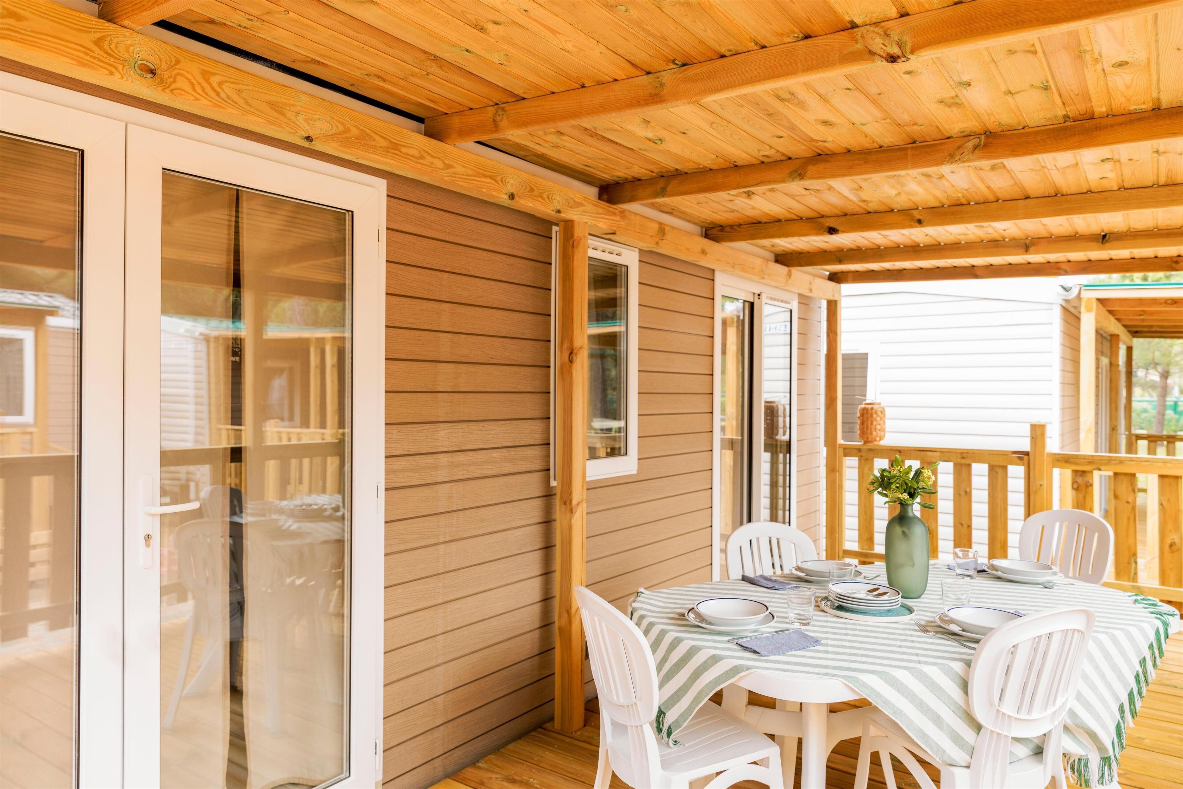 Une terrasse couverte avec un plafond en bois, une table dressée pour le repas et une vue sur les environs.