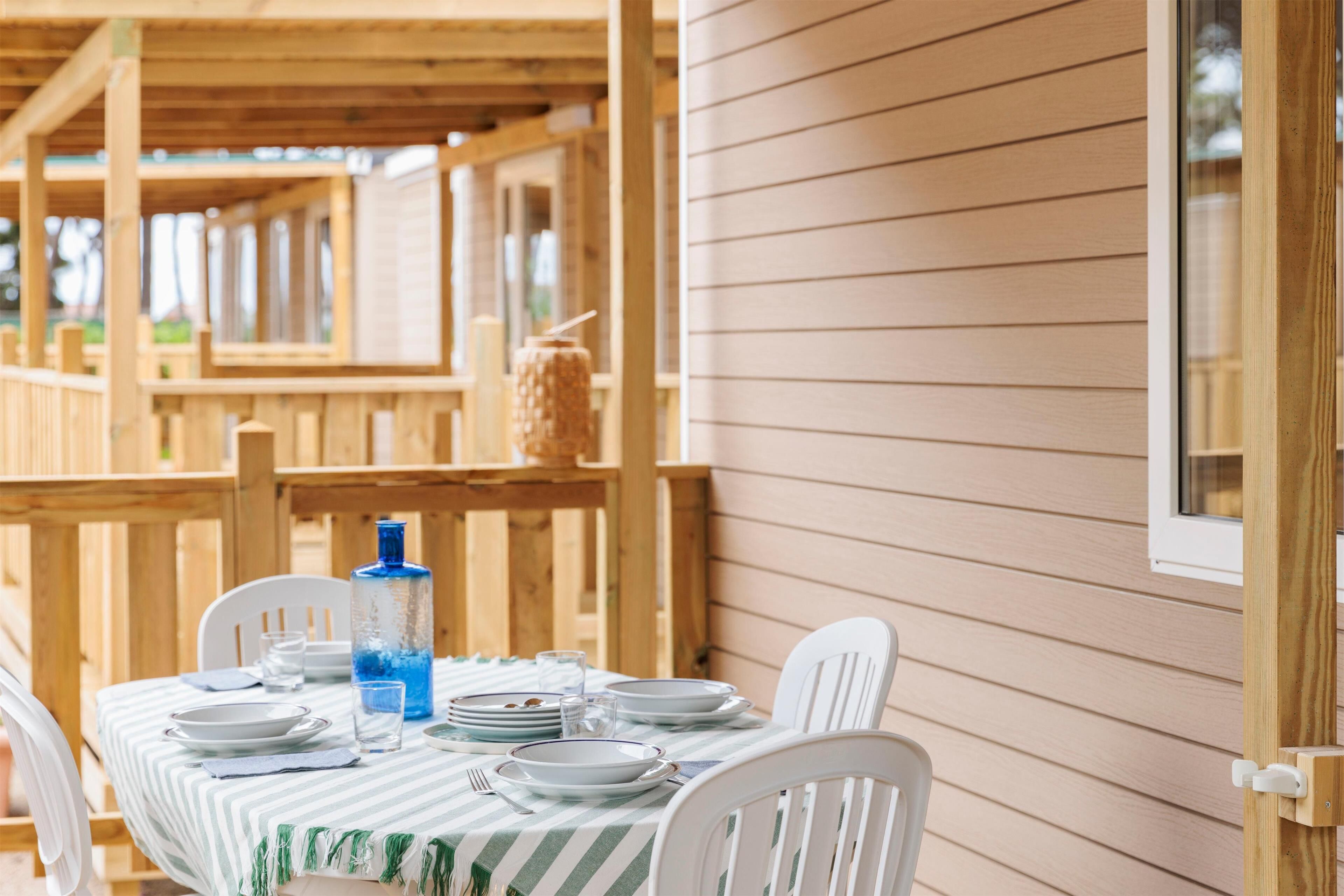 A wooden deck with a table set for dining, featuring striped tablecloths and white chairs.