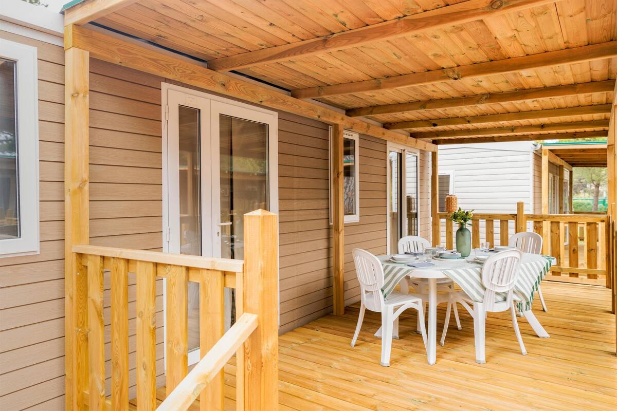Un espace extérieur abrité, doté d’une terrasse en bois, d’une table avec des chaises et d’une rambarde.