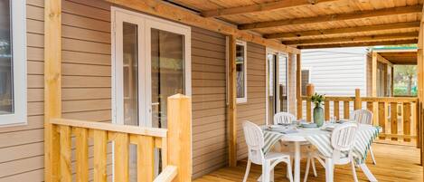 A covered outdoor area with a wooden deck, a table with chairs, and a railing.