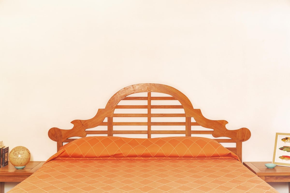 Un lit avec une tête de lit en bois, une couvre-lit à motifs orange et un globe sur une table de chevet.