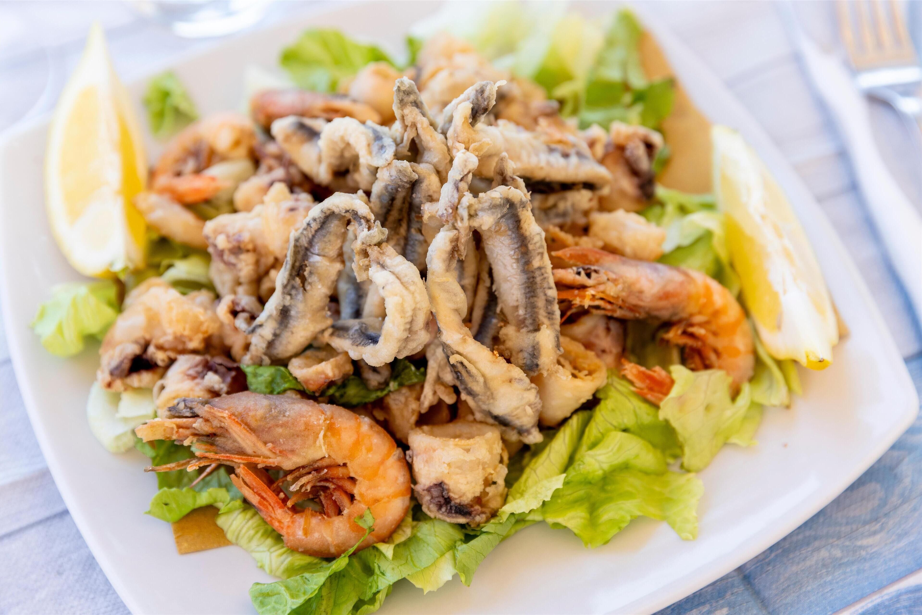 Un plato de mariscos, con camarones y calamares, servido sobre una cama de lechuga y acompañados de gajos de limón.