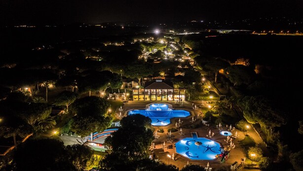 Un gran complejo turístico con múltiples piscinas, un edificio central y zonas ajardinadas circundantes.