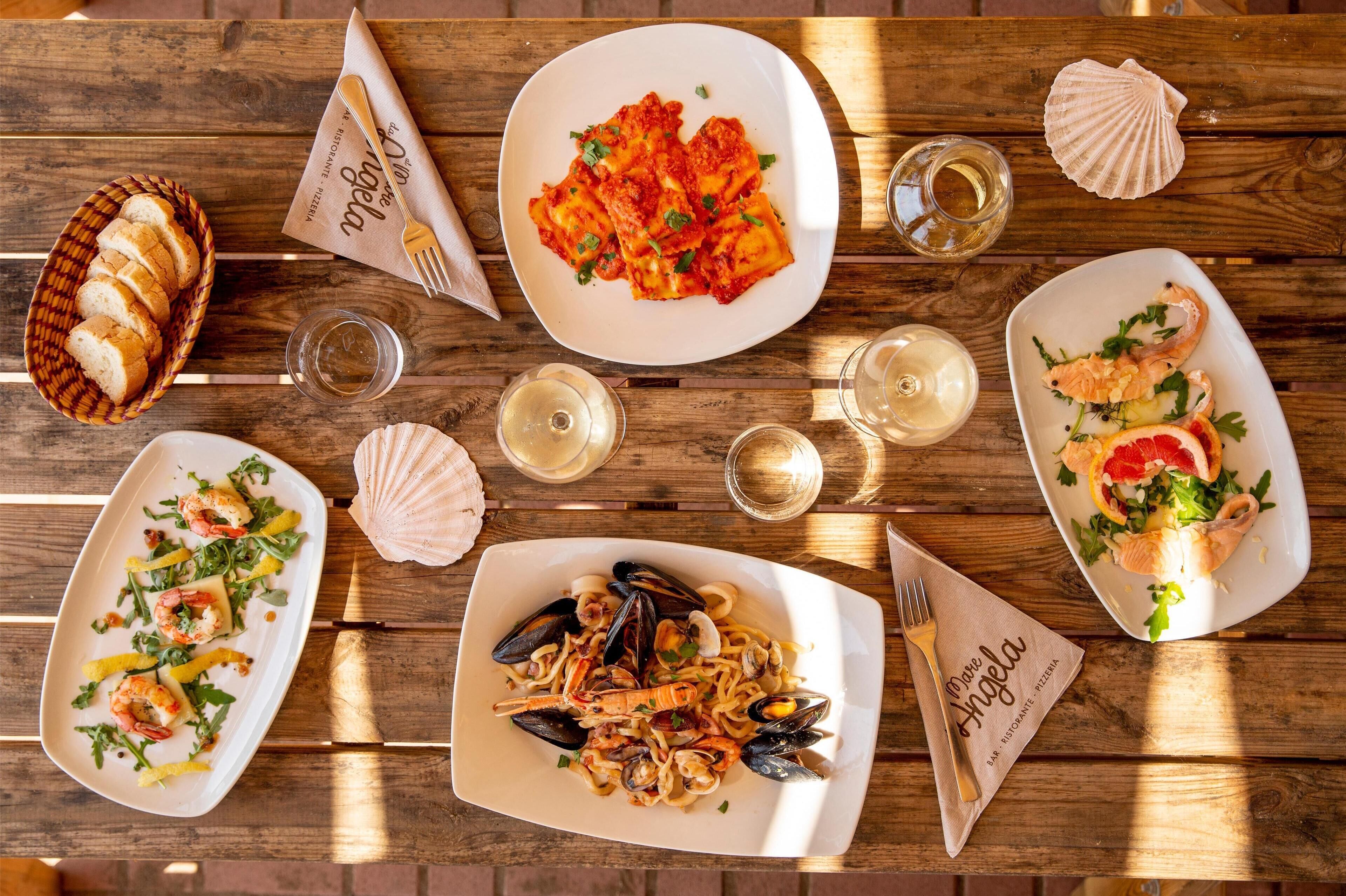 A wooden table with various dishes, including seafood pasta and a seafood salad.