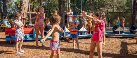 A group of children playing in an outdoor area with trees and a playground.